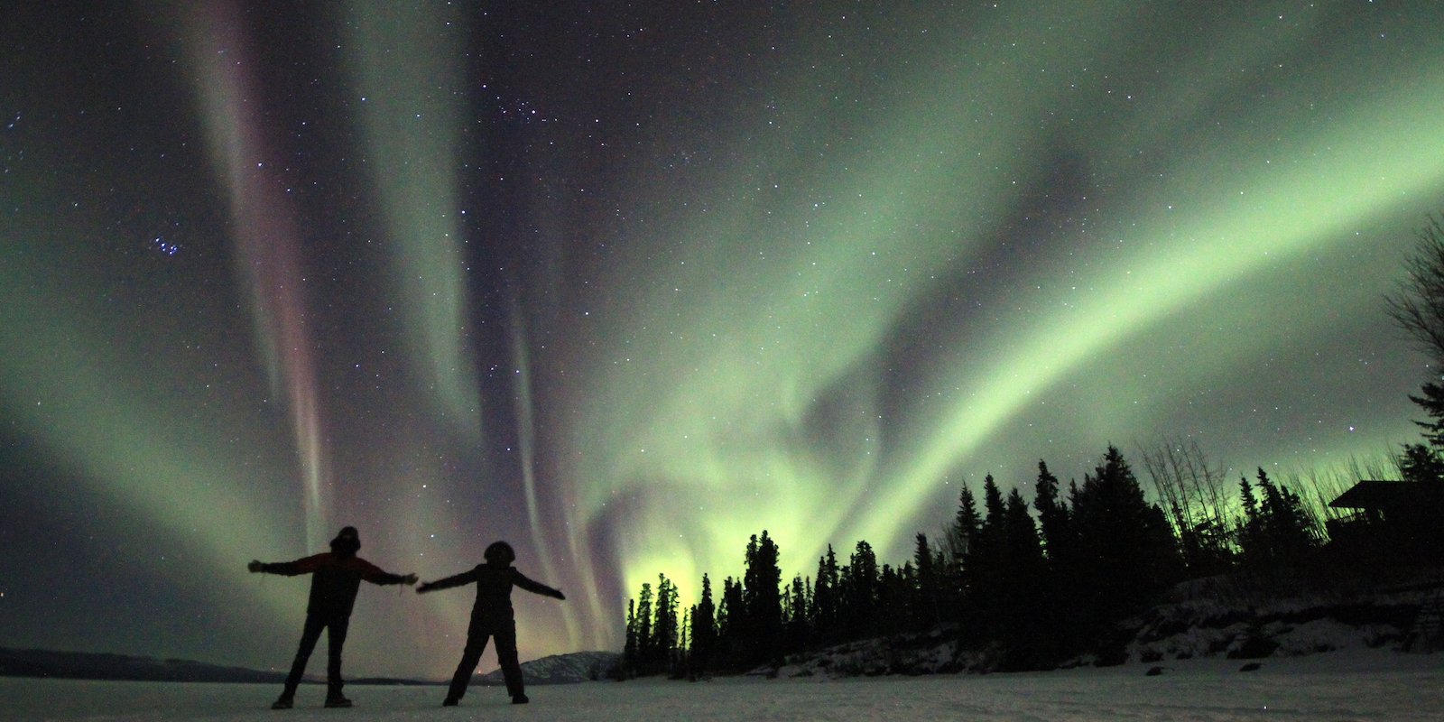 Two people on a frozen lake enjoying the northern lights in Whitehorse Yukon, Canada